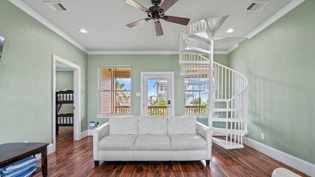 Sala de estar con sofá blanco, piso de madera, ventilador de techo y escalera en espiral blanca.