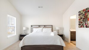 Un dormitorio con una cama grande, dos mesitas de noche con lámparas, una lámpara de pared y vistas al exterior a través de una ventana.