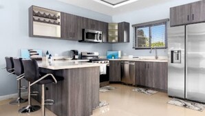 A modern kitchen with a central island, built-in appliances, and bar stools. - Private Cottage in Drax Hall Manor Pool Gym 24hr Secure (Ocho Rios)