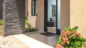 A modern building with a stone pillar, a glass door entrance, and a small outdoor seating area with a bench and a table. - Private Cottage in Drax Hall Manor Pool Gym 24hr Secure (Ocho Rios)