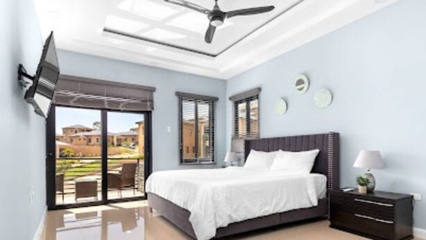 A bedroom with a bed, a nightstand, a TV mounted on the wall, and a ceiling fan. - Private Cottage in Drax Hall Manor Pool Gym 24hr Secure (Ocho Rios)