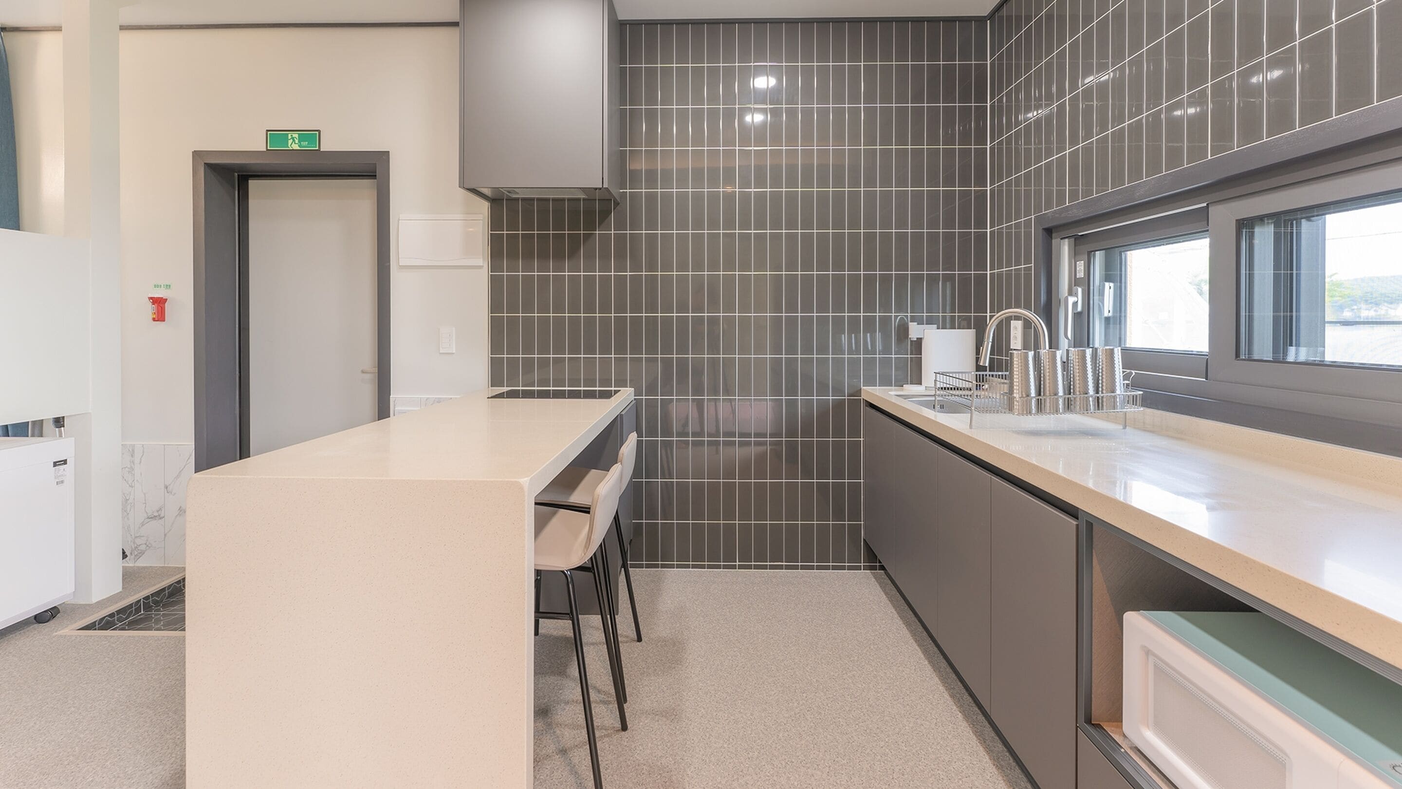 A modern kitchen with a central island, grey tiled backsplash, and a window providing natural light.