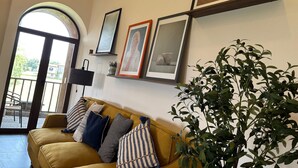 A living room with a yellow sofa, framed artwork on the wall, and a potted plant.