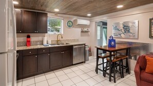 A kitchen with dark wooden cabinets, a white refrigerator, a sink, and a countertop with a coffee maker. There is a dining area with a table and chairs, and a wall-mounted air conditioner. - Lakefront Fishing Retreat w/ Dock, Hot Tub & Deck Views (Sunrise Beach)