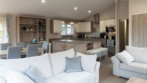 A modern kitchen with a central island, built-in cabinets, and a dining area with a table and chairs. - Bittern Lodge: 3BD Retreat in South Lakeland Park (Borwick)