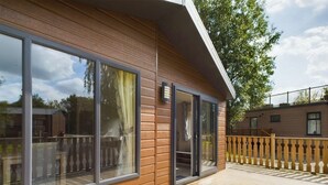 A wooden deck with large windows and a wooden railing. - Bittern Lodge: 3BD Retreat in South Lakeland Park (Borwick)