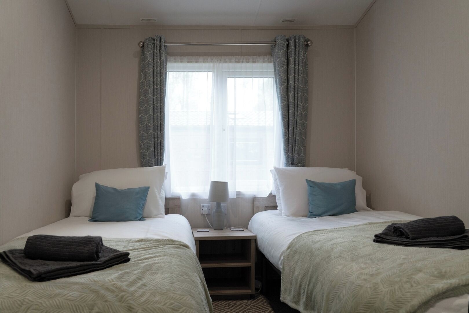 Une chambre d’hôtel avec deux lits, une table de chevet, une lampe et une fenêtre avec des rideaux.
