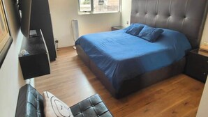 Une chambre avec un grand lit, une télévision, une fenêtre et un petit coin salon.