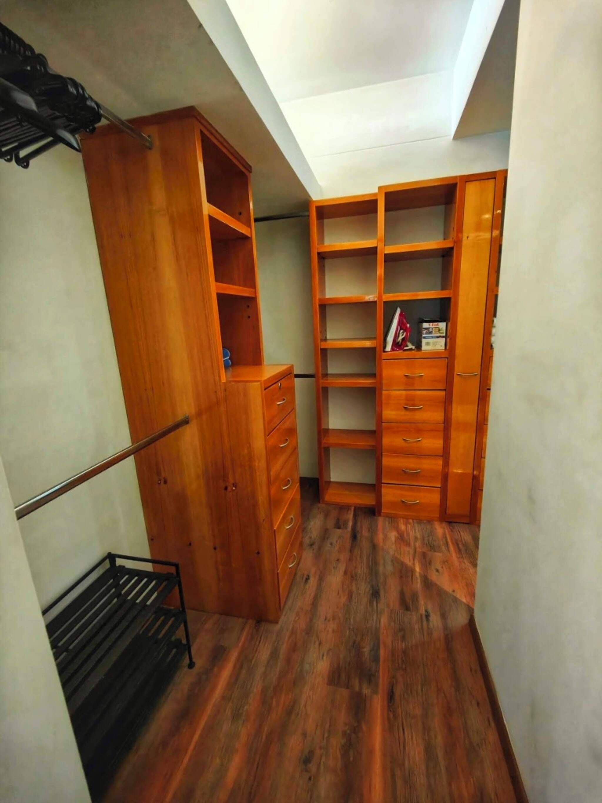 A small, narrow closet with wooden shelving and drawers, a metal rack, and a skylight above.