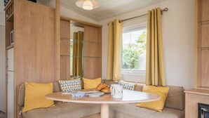 Une pièce de taille modeste comprenant une table à manger, deux coins salon avec des sièges confortables, une fenêtre avec des rideaux et un miroir.