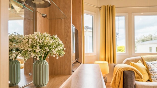 Une chambre d’hôtel moderne avec un plancher en bois, un canapé avec des coussins jaunes, une petite table avec une lampe et une grande fenêtre avec des rideaux.