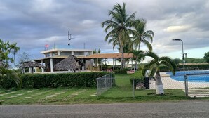 A resort with a pool, palm trees, and a thatched-roof structure.