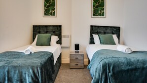 A hotel room with two beds, each with a green bedspread and matching pillows, a small bedside table with a lamp, and two framed abstract art pieces on the wall. - Cosy Wigan Apartment With Sunny Views (Wigan)