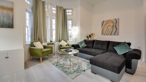A modern living room with a grey sofa, green armchairs, a glass coffee table, and a marble-patterned rug. - Cosy Wigan Apartment With Sunny Views (Wigan)