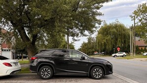 A black SUV parked on a residential street with houses and trees in the background.