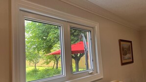 A room with a large window overlooking a backyard with a red umbrella and a tree.