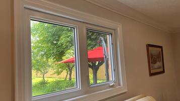 A room with a large window overlooking a backyard with a red umbrella and a tree.
