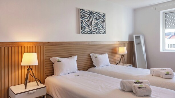 A hotel room with two beds, a wooden headboard, a bedside lamp, a bedside table, a mirror, and a wall art piece. - Priolo’s Nest - Sunlit Retreat with Free Parking (Unknown)