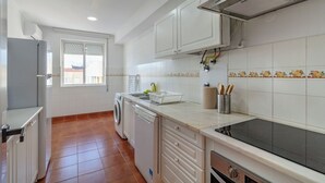 A kitchen with white cabinets, a dishwasher, a stove, and a window with a view of buildings outside. - Priolo’s Nest - Sunlit Retreat with Free Parking (Unknown)