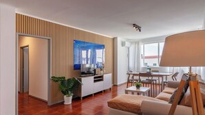 A modern living room with a sofa, a dining table, and a TV. There is a plant and a lamp. - Priolo’s Nest - Sunlit Retreat with Free Parking (Unknown)