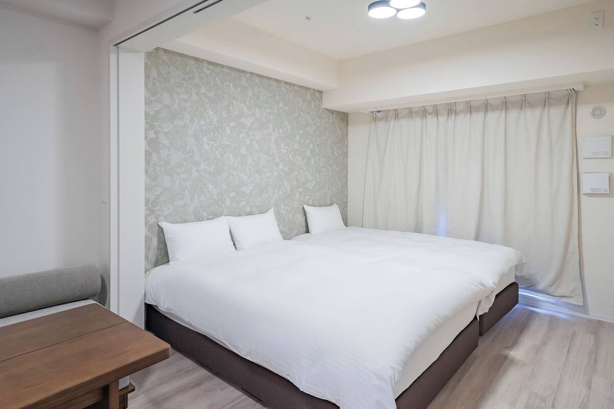 A modern bedroom with a large bed, a wooden nightstand, and a textured wall.