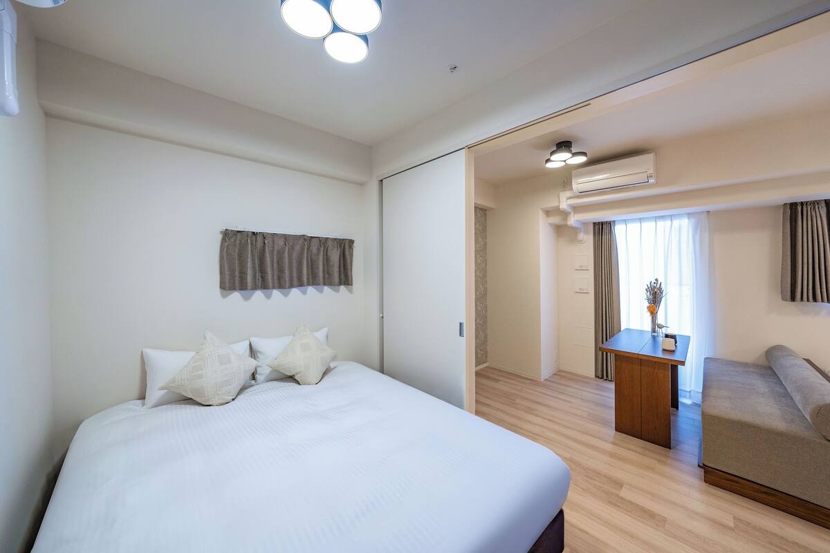 A hotel room with a large bed, a desk, a sofa, and an air conditioning unit.