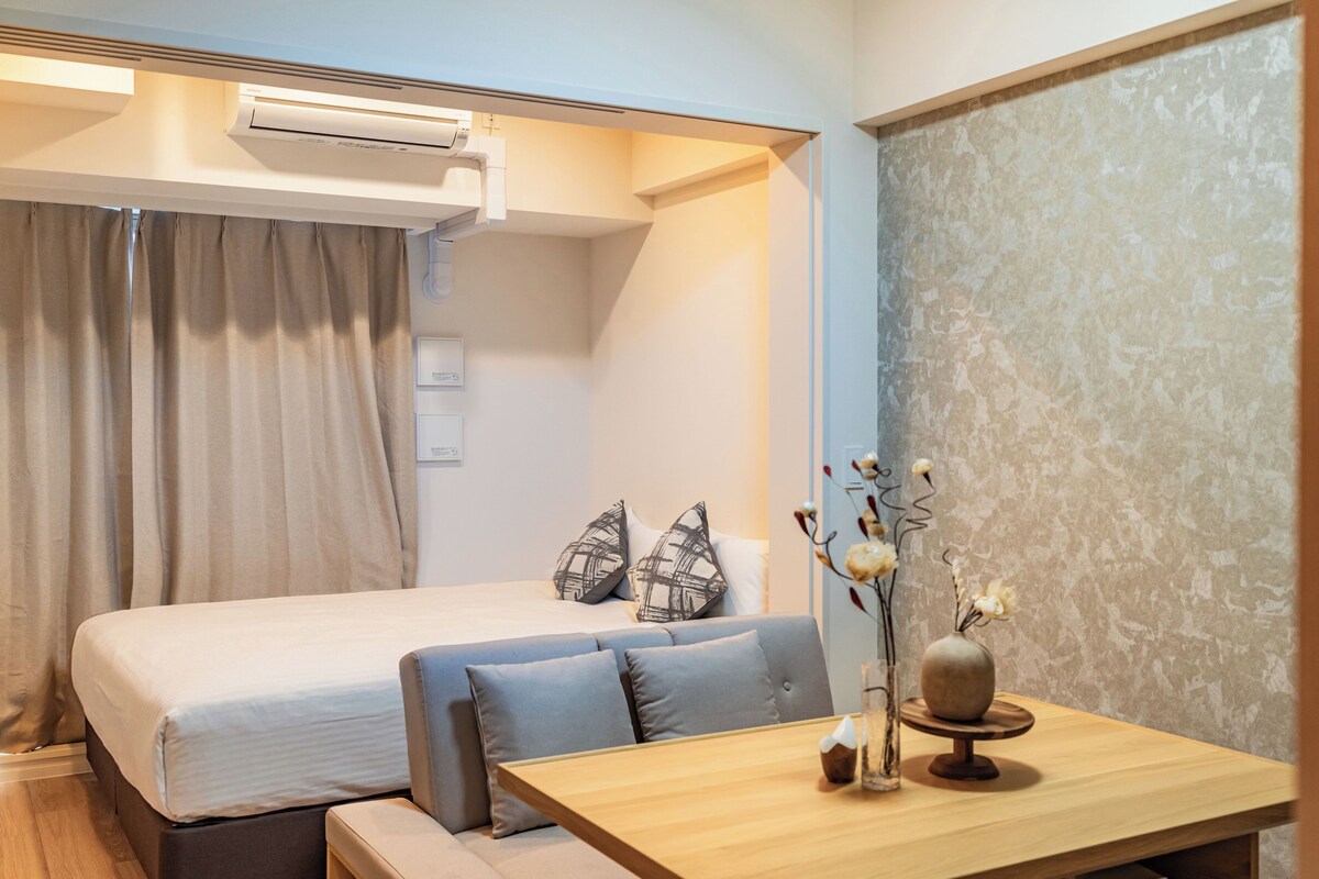 A hotel room with a bed, a sofa, a wooden table, and a vase with flowers.