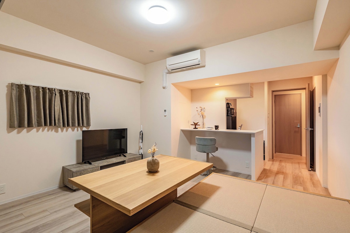 Una sala de estar moderna con una mesa de madera, un televisor de pantalla plana, un sofá y un pequeño jarrón decorativo.