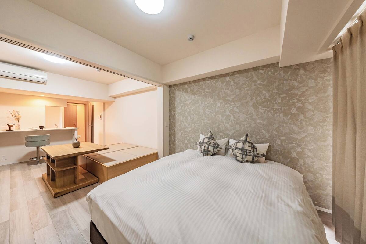 A modern hotel room with a large bed, a desk with a chair, a small seating area, and a bathroom visible through an open door.