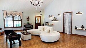 Uma sala de estar ampla com um sofá branco em formato de L, uma poltrona de madeira escura e uma mesa de centro de madeira com objetos decorativos.