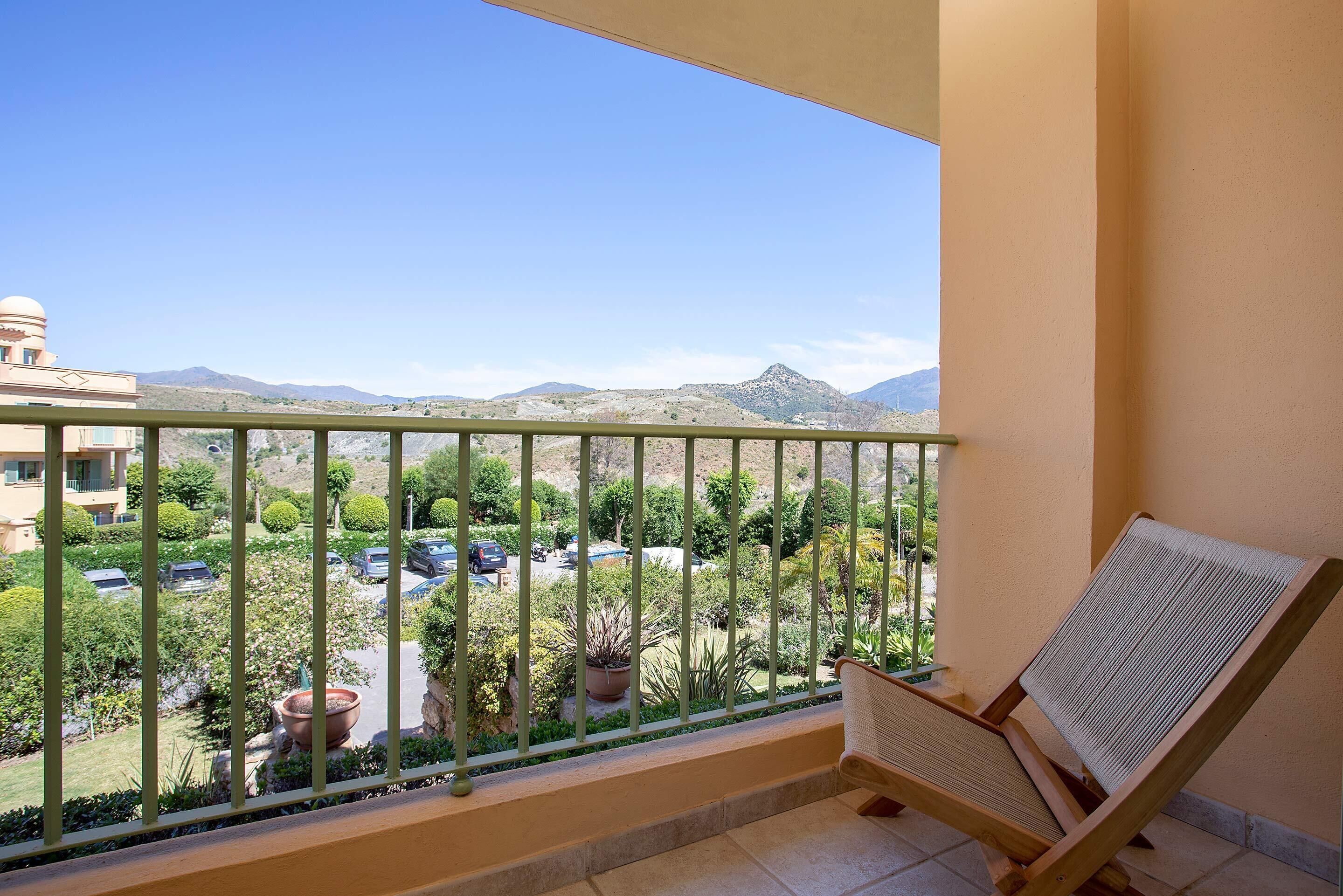 A balcony with a view of a parking area and mountains.