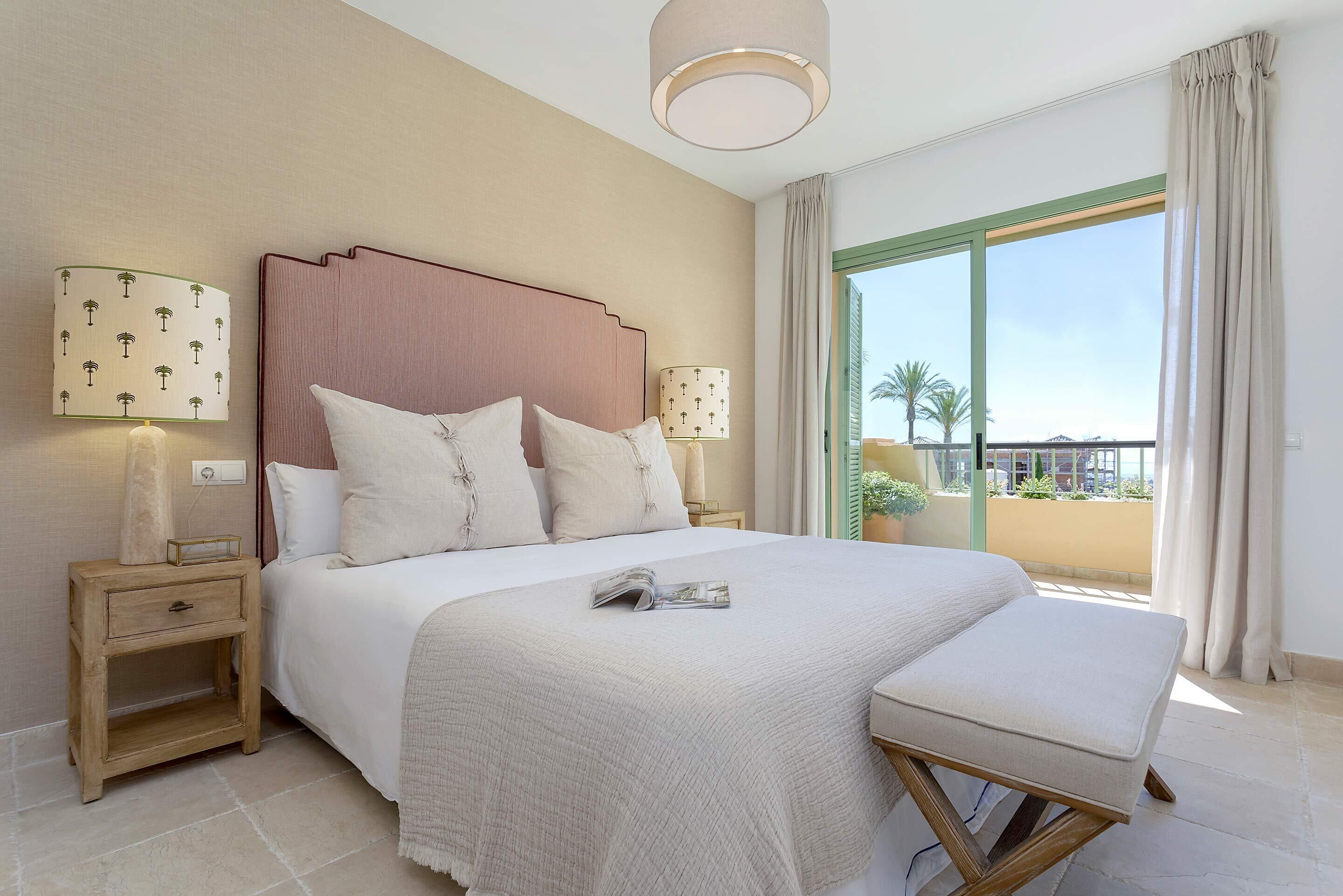 A hotel room with a large bed, two bedside lamps, a nightstand, a window with a view, and a balcony.