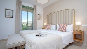 A hotel room with a large bed, a bench, a bedside table with a lamp, and a view of the outdoors. - Genteel Home Flamingos Golf (Seville)