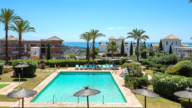 A pool area with lounge chairs and umbrellas, surrounded by palm trees and a view of the sea. - Genteel Home Flamingos Golf (Seville)