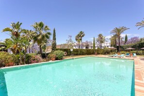 A swimming pool with surrounding palm trees and a clear blue sky. - Exclusive 2BD apartment heated pool. Flamingos Golf (Seville)