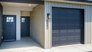A modern garage with a dark door and a light-colored exterior wall. - 2BR/2.5BA 15 Min. Silverwood,  9 Min. Hayden Lake (Hayden)