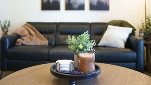 A living room with a black leather sofa, a small round table with a tray holding a candle, a plant, and a remote control. - 2BR/2.5BA 15 Min. Silverwood,  9 Min. Hayden Lake (Hayden)