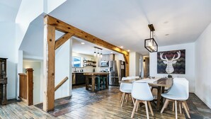 Un'ampia cucina con elettrodomestici moderni, una zona pranzo in legno con sedie bianche e un quadro di grandi dimensioni appeso al muro.