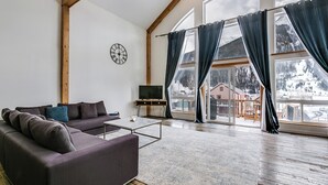 Un soggiorno moderno con divano, tavolino e televisore. Ampie finestre con tende offrono vista su un paesaggio innevato.