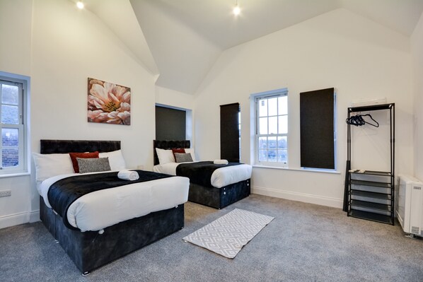 Une chambre avec deux lits, une grande fenêtre, un radiateur et un porte-manteau noir.