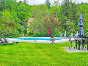 Une piscine entourée d’une pelouse verdoyante, avec des chaises longues et des parasols.