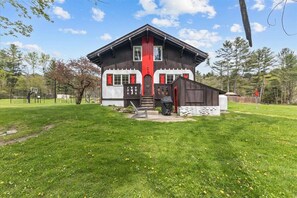 Une maison à deux étages, avec une façade rouge et blanche, un porche à l’avant et un petit jardin.