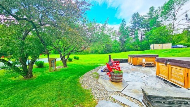 A backyard with a stone patio, a fire pit, wooden benches, and a grill area.