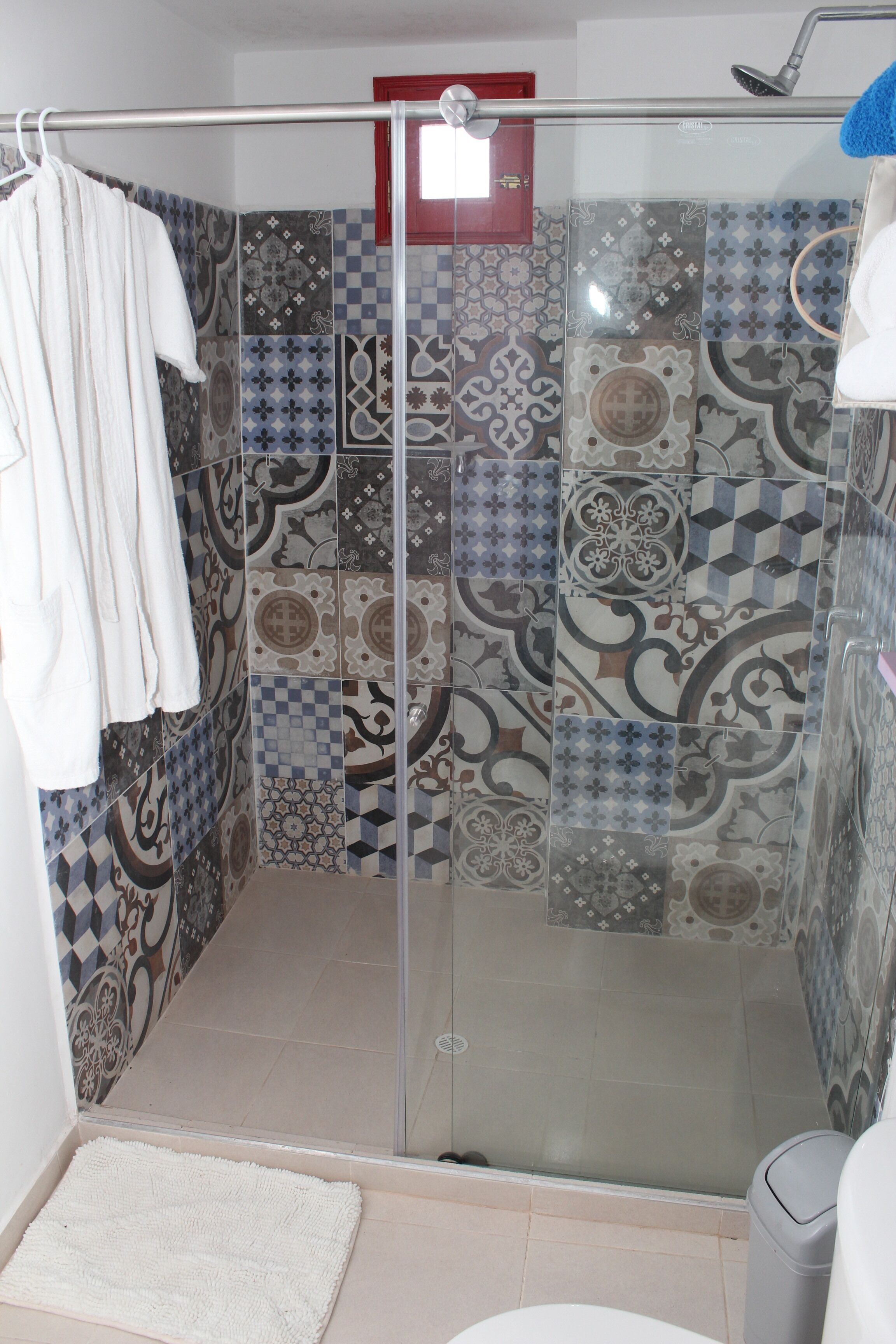 A shower with patterned tiles, a glass door, and a white towel hanging on a rack.