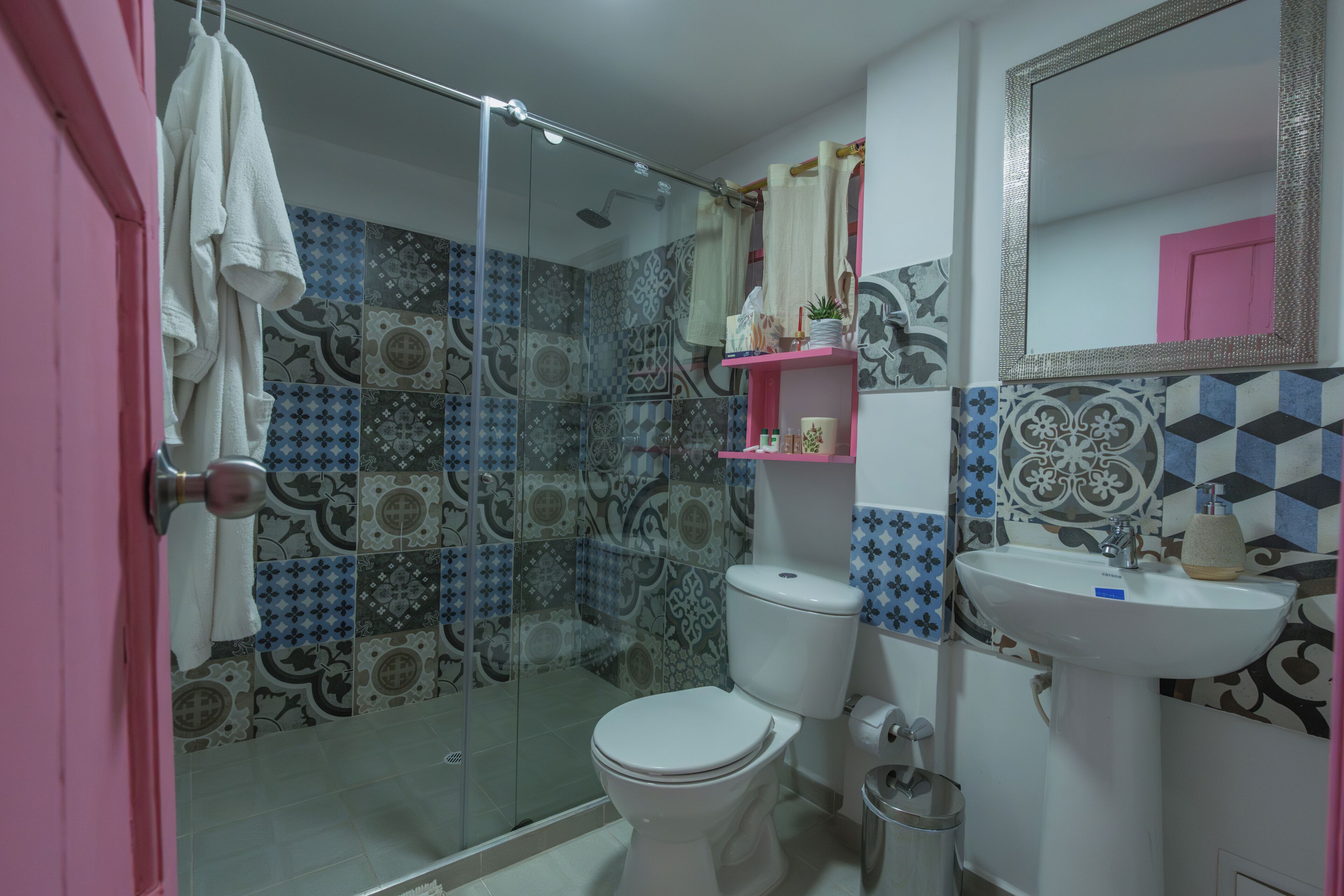 A bathroom with a shower, toilet, sink, and a pink door.