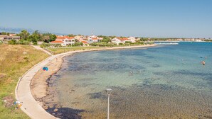 Et kystområde med klart vand, en sandstrand og boliger med røde tage.
