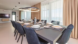 En moderne spisesal med et langt bord dækket til seks personer, præget af et minimalistisk design med mørke stole og en central lysekrone.