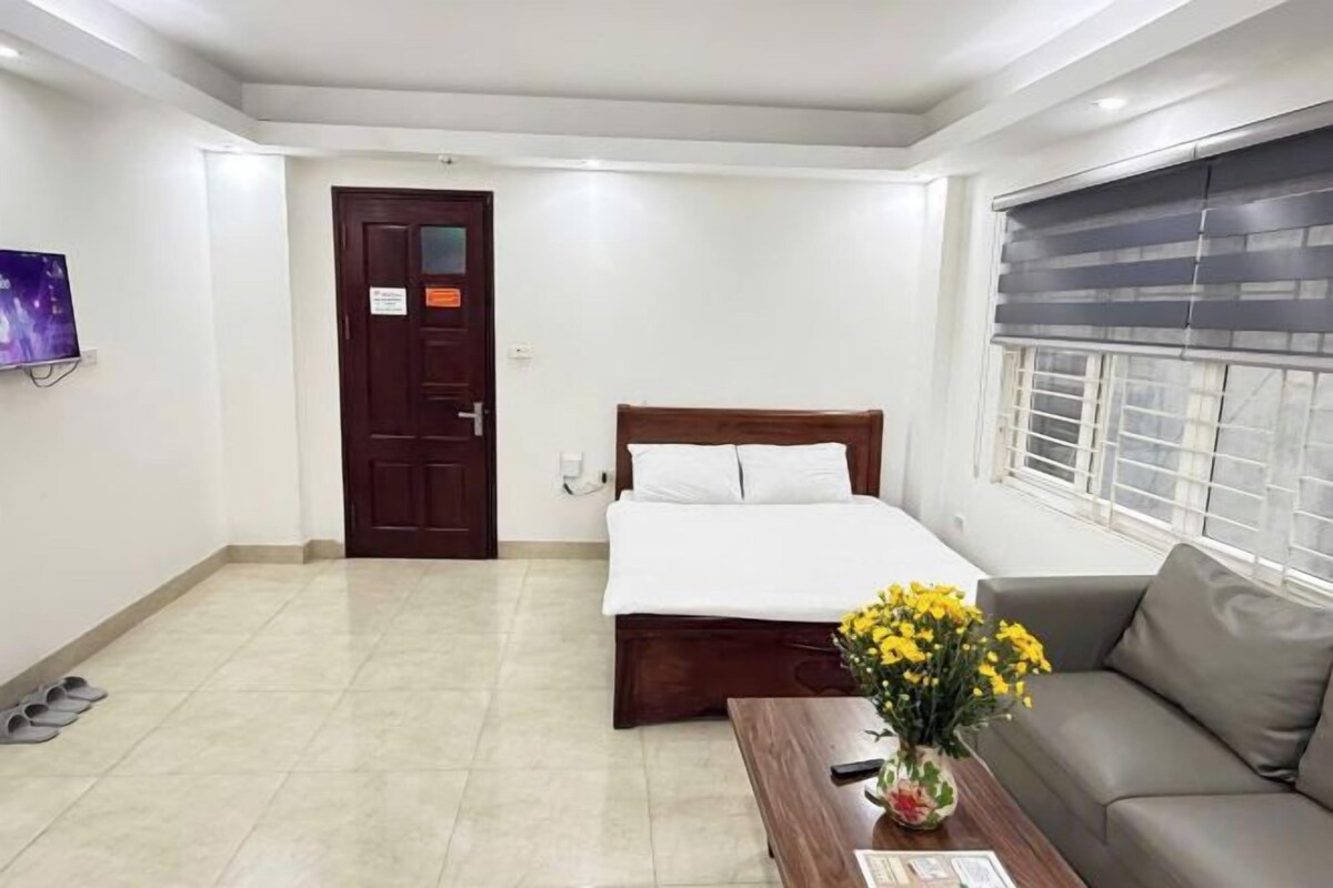 Quarto de hotel com cama, sofá, televisão, janela com persianas e porta.
