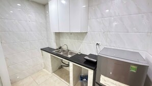 Una cocina compacta con baldosas de mármol blanco, encimera negra, pileta de acero inoxidable y refrigerador.