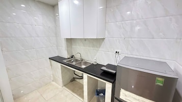 Cozinha compacta com azulejos de mármore branco, bancada preta, cuba de aço inoxidável e geladeira.
